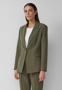 Blazer entallado en verde oliva, hecho de una tela suave, que presenta un cierre de un solo botón, cuello de solapa y dos bolsillos frontales.