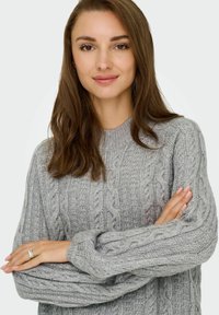 Sivi pulover od pletenine s okruglim izrezom i dugim rukavima. Tekstura je mekana, s uzdignutim uzorcima duž tkanine.