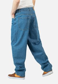 Jeans holgados azules de mezclilla, con un corte relajado, dos bolsillos traseros y un parche de cuero marrón en la cintura.