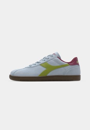 Light blue suede sneaker with a green logo, pink accents on the heel, and a brown rubber sole featuring a textured design.