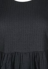 Robe noire texturée avec un col rond, présentant un motif froissé et une jupe tiered froncée. Tissu lisse partout.