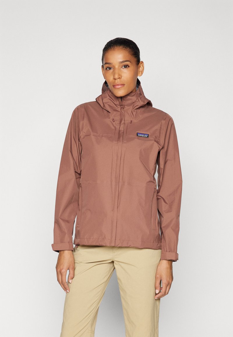 Chaqueta impermeable marrón con capucha, cremallera frontal y bolsillo en el pecho. El material parece ligero y suave, diseñado para uso al aire libre.