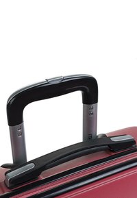 Maleta roja con una superficie texturizada, que cuenta con un asa superior de plástico negro y un mango telescópico de aluminio plateado con botón de liberación.