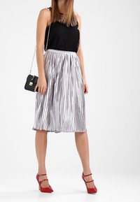 Czarny top na ramiączkach z koronkowym wykończeniem w zestawieniu z srebrną, plisowaną spódnicą midi. Czerwone szpilki. Mała czarna torebka na ramię z łańcuszkowym paskiem.