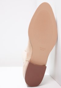 Suela de zapato de mujer de ante beige con tacón, con agarre texturizado y texto "Hecho en España" visible sobre un fondo blanco.