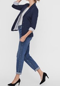 Marinblazer med uppvikt ärm, vitrandig foder, tillsammans med ljusblå upprullade jeans och svarta högklackade skor.