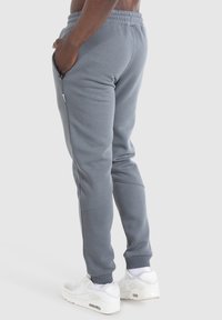 Pantalones deportivos grises con diseño ajustado, cintura elástica, bolsillos laterales y puños acanalados, combinados con zapatillas deportivas blancas.