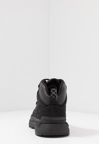 Bottines noires montantes en cuir suédé et matériaux synthétiques, avec un design à lacets et une semelle en caoutchouc texturé.