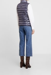 Vadderad grå väst med horisontellt quiltat mönster, kombinerad med ljusblå vida jeans och bruna stövlar med ormskinnsmönster och klack.