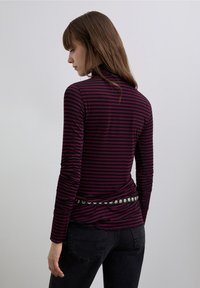 Long-sleeve top in dark burgundy and black horizontal stripes, featuring a mock neck and a fitted design, paired with black jeans and a studded belt.