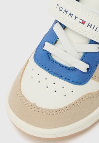 Baskets avec une tige en cuir blanc et des accents en daim beige, des superpositions en synthétique bleues, des lacets blancs et une sangle de marque.