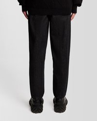 Juodi džinsiniai kelnių su tiesiu siluetu ir subtiliu tekstūru, su užpakalinėmis siūlėmis, vilkėti su masyviais juodais batais.