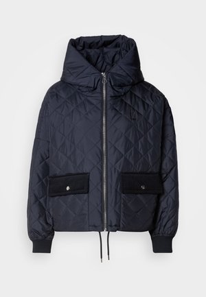 Giacca trapuntata navy con un ampio cappuccio, zip frontale e due grandi tasche in corduroy nere. Presenta polsini elastici e un orlo con cordino.