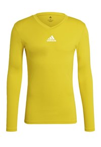 Langsleeve geel sportshirt van gladde stof. Heeft een V-hals en een wit Adidas-logo dat gecentreerd op de borst is.