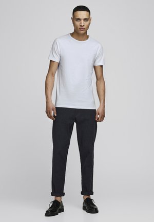 Weißes Kurzarm-T-Shirt mit Rundhalsausschnitt, kombiniert mit dunkel gemusterten Hosen und schwarzen Lederschuhen. Einfaches, lässiges Outfit.