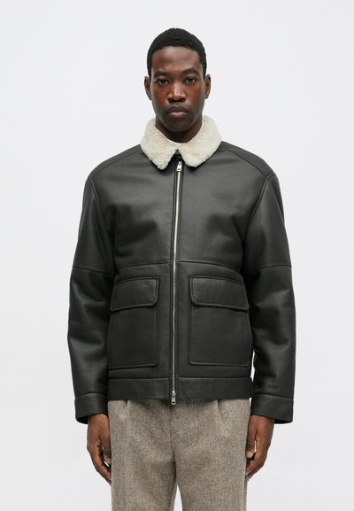 Čierna kožená bunda s kožúškovým golierom, s predným zipsom, dvomi prednými vreckami a hladkou textúrou. Jednoduchý, štruktúrovaný dizajn.