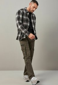 Koszula flanelowa w kratę w kolorze czarnym, szarym i białym; czarny t-shirt z okrągłym dekoltem; oliwkowe spodnie cargo z kieszeniami; szare sneakersy z białymi akcentami.