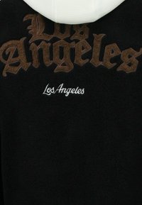 Zwarte fleece hoodie met grote, bruine Gotische "Los Angeles"-tekst en kleinere witte "Los Angeles"-tekst. Witte binnenkant van de capuchon.