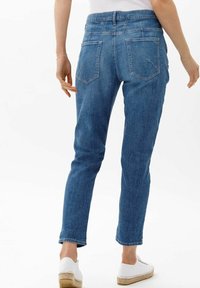 Jeans de mezclilla azul con pierna estrecha, cintura de media altura y dos bolsillos traseros. La tela tiene una textura suave y un lavado clásico.