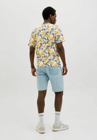 Tricou floral pentru bărbați cu flori galbene pe un fundal alb, asortat cu pantaloni scurți din denim de culoare albastră deschisă. Are mâneci scurte și decolteu rotund.