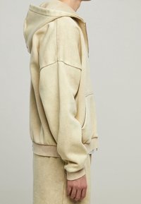 Felpa beige con zip realizzata in tessuto morbido, dal taglio relaxed, con un ampio cappuccio e polsini e orlo a costine.