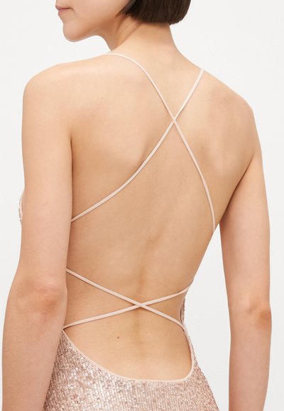 Takaktsyn av en utenermet kjole med paljettdesign, med tynne nylonstriper som krysser hverandre og en dyp utskåret rygg i en myk rosefarge.