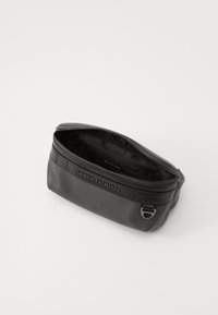 Pochette in pelle nera con una texture liscia, chiusura con zip e nome del marchio impresso. L'interno presenta un motivo a logo ripetuto. Design compatto.