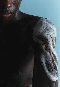 Czarna skóra o piankowej fakturze pokrywająca ramię, na tle jasno niebieskim. Zbliżenie podkreślające kształty i kontrasty.