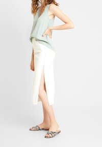 Haut sans manches en bleu sarcelle avec décolleté en V, associé à une jupe en denim blanche avec de hautes fentes latérales et un ourlet effiloché. Sandales mules à imprimé serpent.