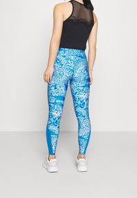 Sinilah leggins biru dengan corak macan tutul, dilengkapi dengan pinggang tinggi dan panel biru solid yang kontras, dipadukan dengan atasan tank mesh hitam.