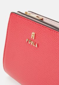 Portefeuille en cuir rouge avec une surface texturée, présentant un logo doré et une bordure noire. Fermeture éclair en haut pour un accès facile.