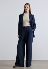 Navy blazer and wide-leg trousers paired with a beige ribbed sweater. Smooth fabric, tailored fit, and subtle side pockets.