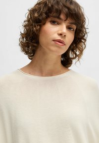 Cream-colored knit top with a round neckline and subtle horizontal texture. Features short, relaxed sleeves and a lightweight feel.