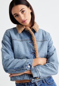 Jeansjacka med en beige, texturerad, fårskinnskrage. Har metallknappar, framfickor och en figurnära design. Blå denim med en blekt finish.