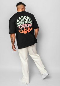 Sort oversized t-shirt med flerfarvet tekst "DROPSIZE CREW LOVE" på ryggen; parret med hvide bukser og sneakers.