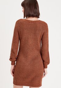 Vestido de punto en color óxido con mangas largas abullonadas, un escote ancho y una silueta ajustada. La textura es acanalada y suave.