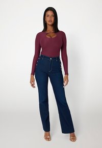 Bordo ilgomis rankovėmis bodis su iškirpte krūtinėje derinamas su aukštu vidumi tamsiai mėlynomis plačiomis džinsomis, puoštomis auksinėmis mygtukų detalėmis.