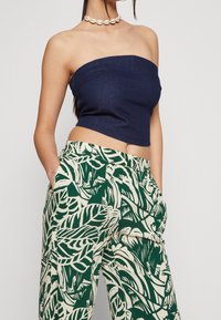 Tmavě modrý bezramenný džínový crop top spárovaný se zelenými a krémovými širokými kalhotami s tropickými listovými vzory a bočními kapsami.