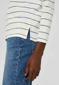 Camicia bianca a maniche lunghe con strisce orizzontali grigie, dotata di spacco laterale. Abbinata a jeans in denim blu, che mostrano una texture liscia.