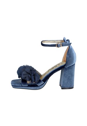 Sandalia de tacón alto de terciopelo azul con correa en el tobillo, tacón ancho y flores decorativas de tela en la correa frontal.