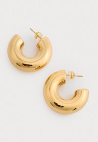 Złote kolczyki w kształcie obręczy o zaokrąglonym, masywnym designie. Gładka faktura z błyszczącym wykończeniem. Bezpieczne zapięcie na post do noszenia.