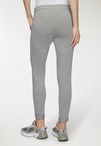 Leggings grigi in miscela di cotone con una vestibilità affusolata, vita elasticizzata e orli arrotolati, abbinati a scarpe da ginnastica grigie e bianche.