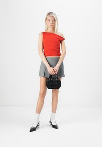 Top rojo de un solo hombro, falda corta gris con plisados, bolso texturizado negro, y tacones negros de puntera afilada con calcetines blancos hasta el tobillo.