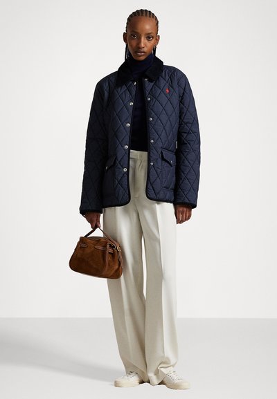 Marineblaue gesteppte Jacke mit einem Cordkragen, silberner Hardware, zwei Fronttaschen, kombiniert mit beigen weiten Hosen und einer braunen Wildleder-Handtasche.