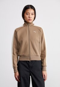 Brown zip-up jacket with high collar, cream side panels, ribbed cuffs, and waistband. Features a small logo on the chest and zippered pockets.