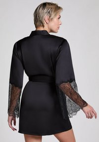 Kimono di raso nero con maniche lunghe e delicati dettagli in pizzo nero, legato in vita. Texture liscia con una finitura lucida.
