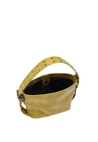 Żółta skórzana torba na ramię z metalowymi ćwiekami na pasku, otwarta góra z czarną podszewką i zapięciem na zatrzask.