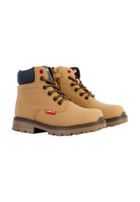 Bottes en cuir tan avec des accents bleu marine, lacets ronds et une étiquette logo rouge. Elles possèdent une semelle robuste avec un embossage prononcé pour une meilleure adhérence.