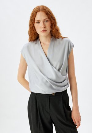 Lys grå, kortærmet bluse med en omslagsdesign og glat tekstur, parret med højtaljede mørke bukser med knapdetalje.