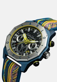 Orologio ottagonale blu con quadrante nero, dettagli gialli e funzioni cronografiche. Il cinturino è in tessuto multicolore e testurizzato.